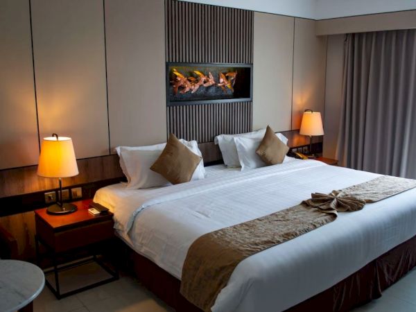 A neatly made hotel room with a king-sized bed, decorative pillows, bedside tables with lamps, and a window with curtains.