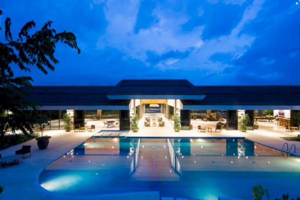 An elegant pool area is seen at dusk, with a modern building in the background, warmly lit and reflecting on the water's surface.