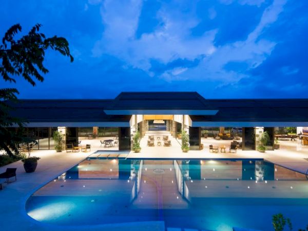 An elegant pool area is seen at dusk, with a modern building in the background, warmly lit and reflecting on the water's surface.
