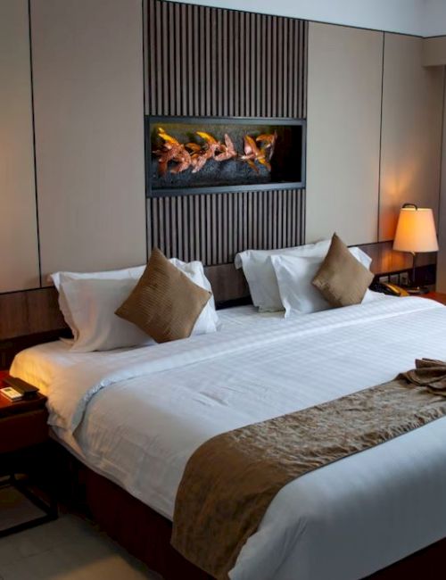A cozy, well-lit hotel room with a large, neatly made bed, bedside tables with lamps, and modern decor, featuring a small wall-mounted fireplace.