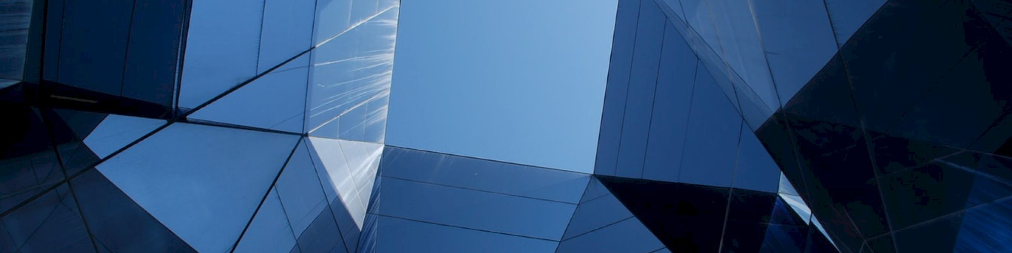 The image shows a symmetrical architectural design with reflective glass panels and a geometric pattern, revealing the blue sky in the center.