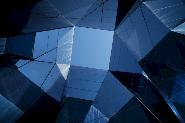 A view looking up at an array of reflective glass building surfaces and windows, forming geometric patterns against the sky.