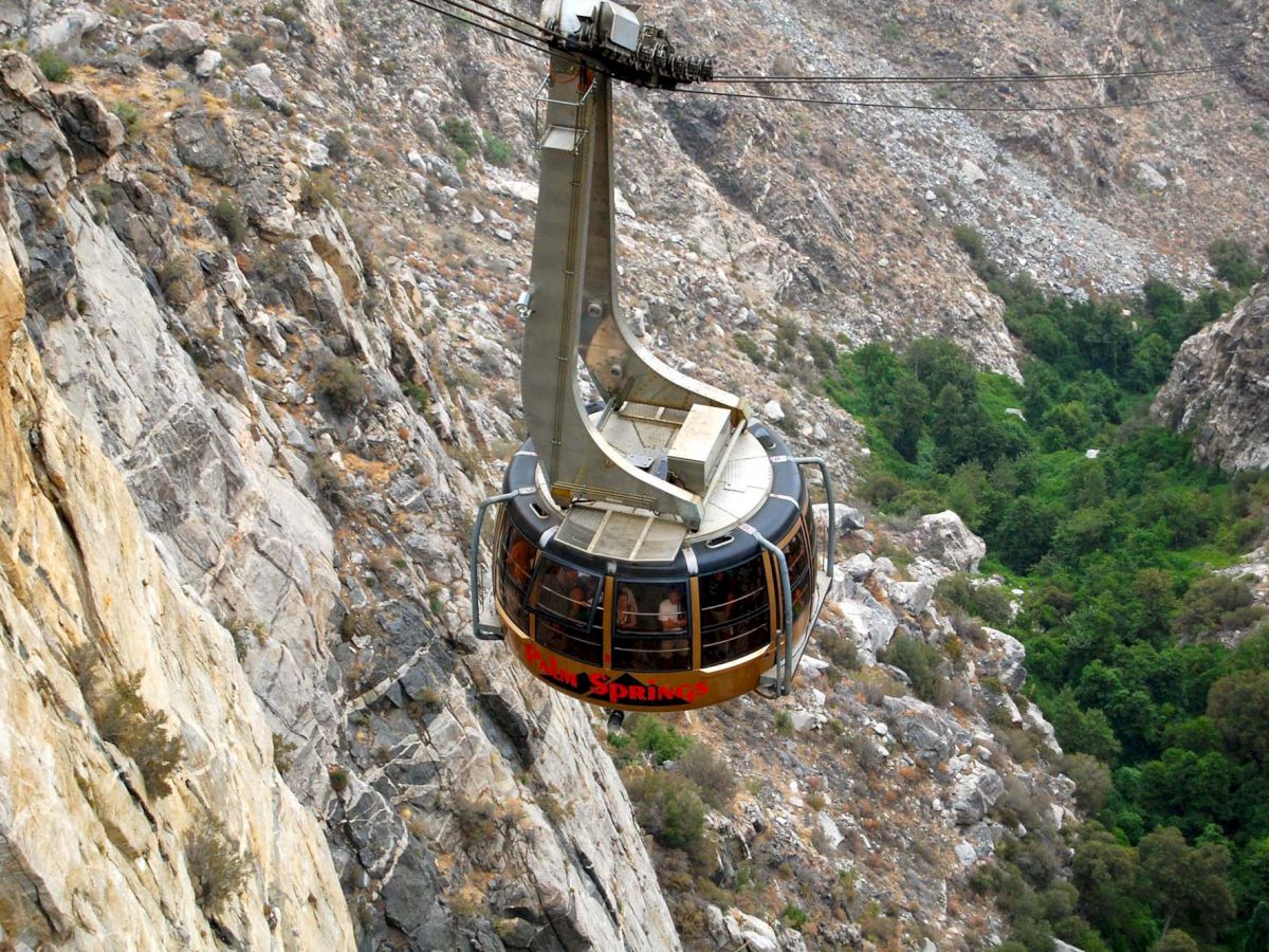 A cable car is suspended over a rocky canyon with greenery below, offering scenic views of the landscape as it travels.