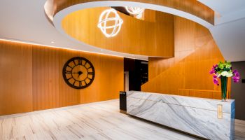This image shows a modern reception area with wood paneling, a large decorative clock, a marble front desk, and a bouquet of flowers on the counter.