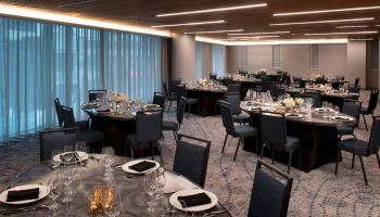 A banquet hall with round tables set with glassware, silverware, and napkins, ready for an event. The room is softly lit and elegantly decorated.