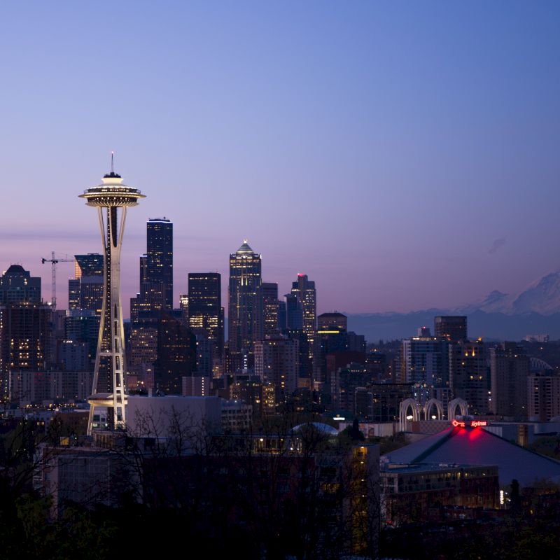 A twilight view of the Seattle skyline, featuring the Space Needle, downtown skyscrapers, and Mount Rainier in the background, ending the sentence.