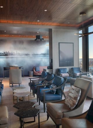 A modern lounge with numerous chairs, large windows offering a scenic view of the waterfront, and a cityscape mural on the back wall.