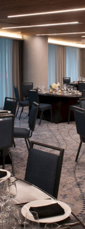 The image shows an elegant banquet room with round tables set for a formal event, featuring neatly arranged place settings, centerpieces, and upholstered chairs.