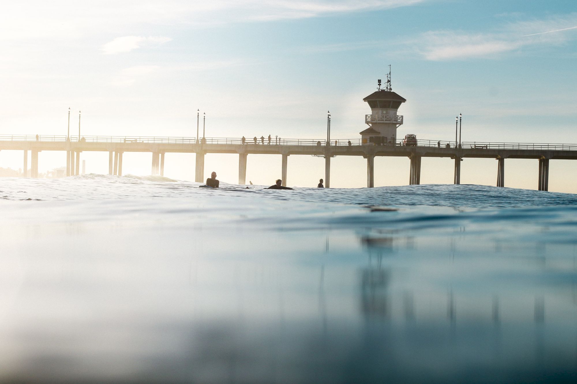 A serene ocean view with people at a pier, featuring a prominent tower and calm waters reflecting the sky's soft hues.
